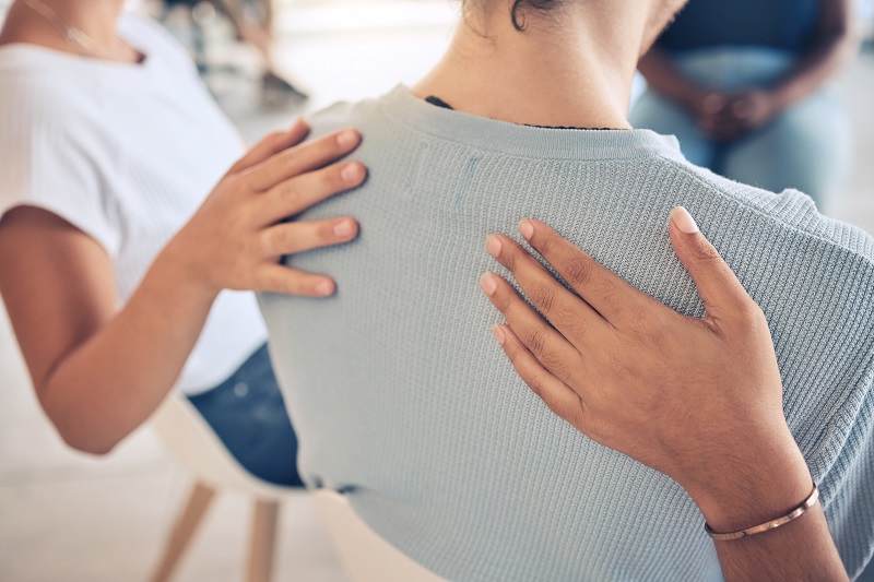 Hands on a woman's back, offering comfort in a support group setting.