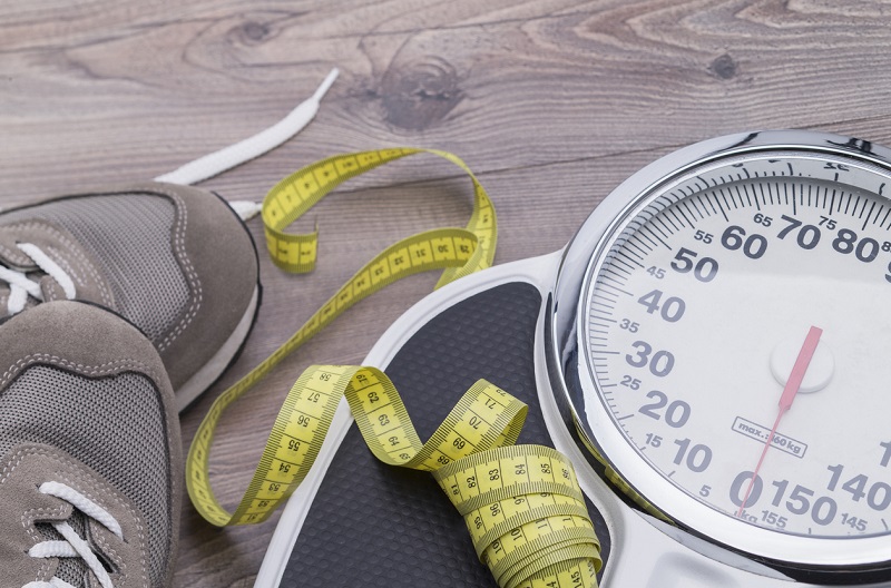 Running shoes with tape measure and scale on a wooden table.