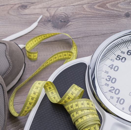 Running shoes with tape measure and scale on a wooden table.