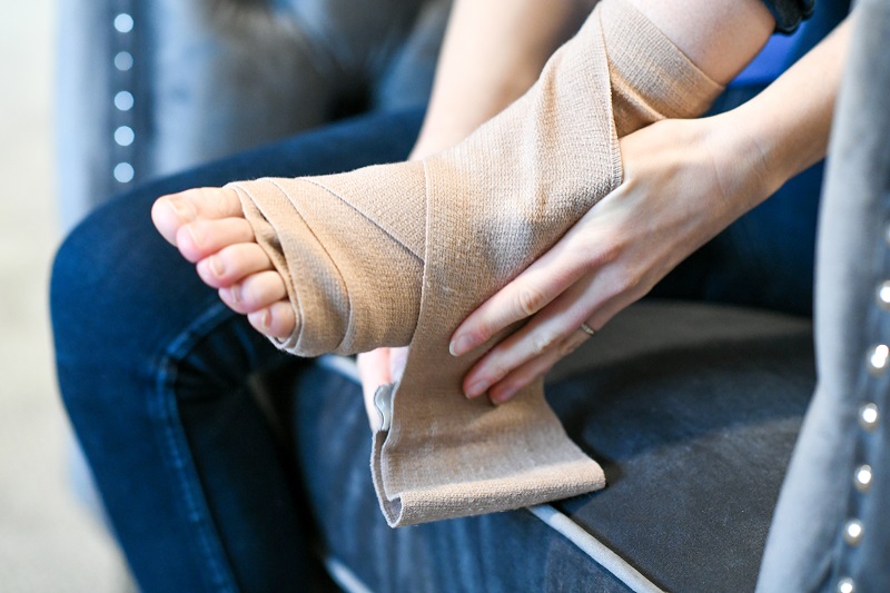 A woman wrapping her ankle with a gauze wrap to rest a sprained ankle.