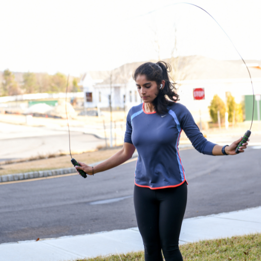 Young woman exercises by jumping rope outdoors.