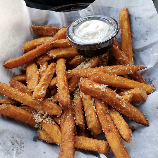 A basket of crisp sweet potato fries with a garlic yogurt dip on the side.