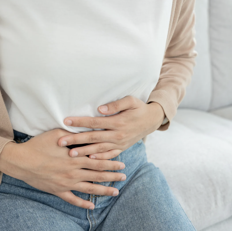 A woman sitting on a couch clutches her abdomen with both hands.