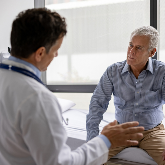 An older man sits and listens as his doctor explains colonoscopy prep.