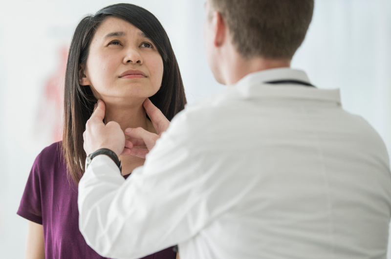  A Caucasian male doctor feels the swollen throat of a female patient.