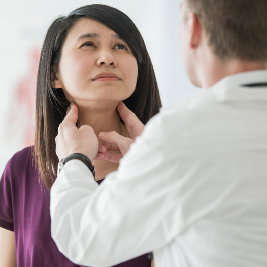  A Caucasian male doctor feels the swollen throat of a female patient.
