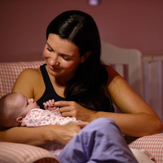 A young mother cuddles her newborn baby in the nursery at night.