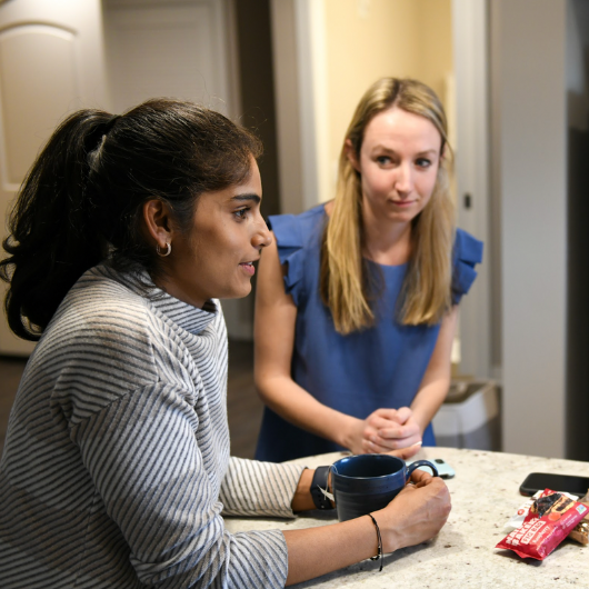 Three young women stand around a kitchen island, chatting.