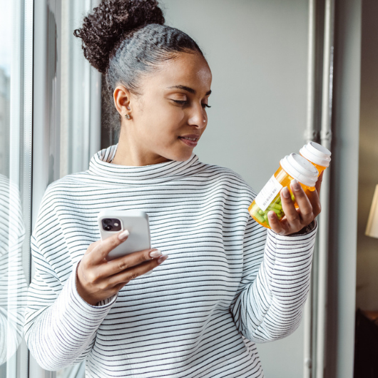 A young woman sits on the sofa researching medicines on her smartphone.
