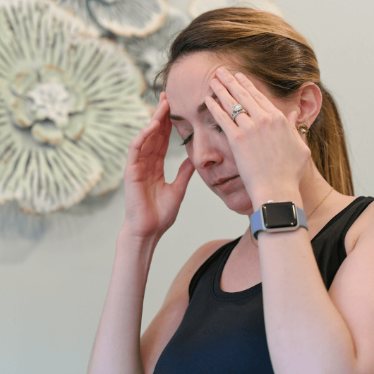 A young woman, who appears to be in pain, presses both hands to her forehead.