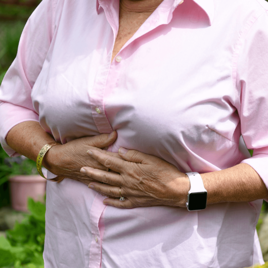 An older woman wearing a pink blouse clutches her upper stomach.