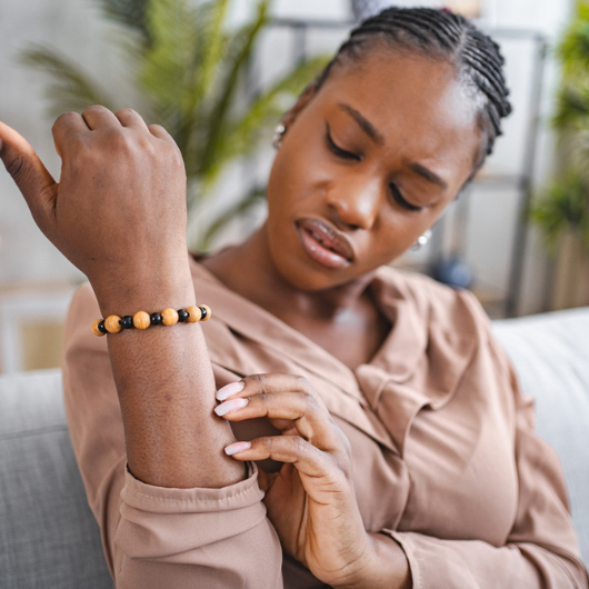 Black woman scratching her itchy skin on her forearm.