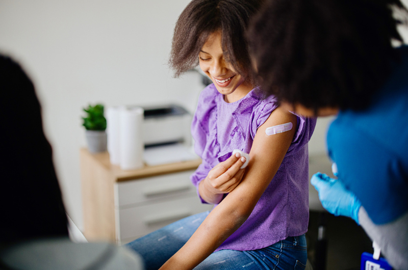 Teen girl getting her HPV vaccine at doctor's office while accompanied by her mother.