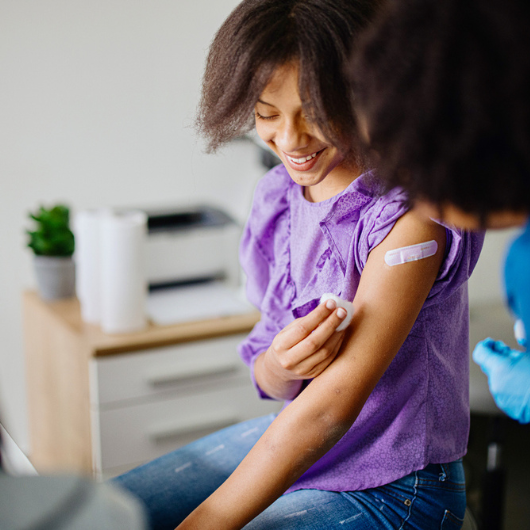 Teen girl getting her HPV vaccine at doctor's office while accompanied by her mother.