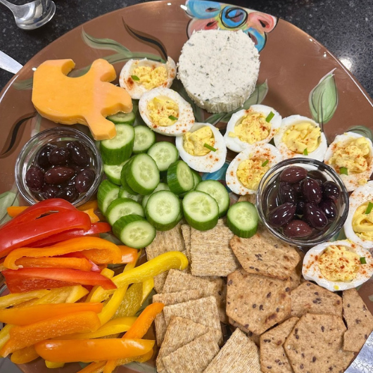 A serving tray full of various crackers, vegetables and deviled eggs.