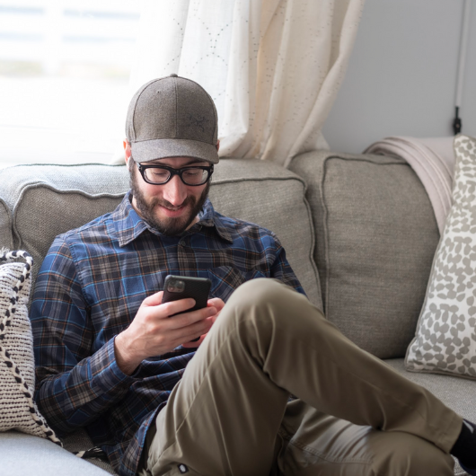 Young man sits on a sofa while texting on his smartphone.