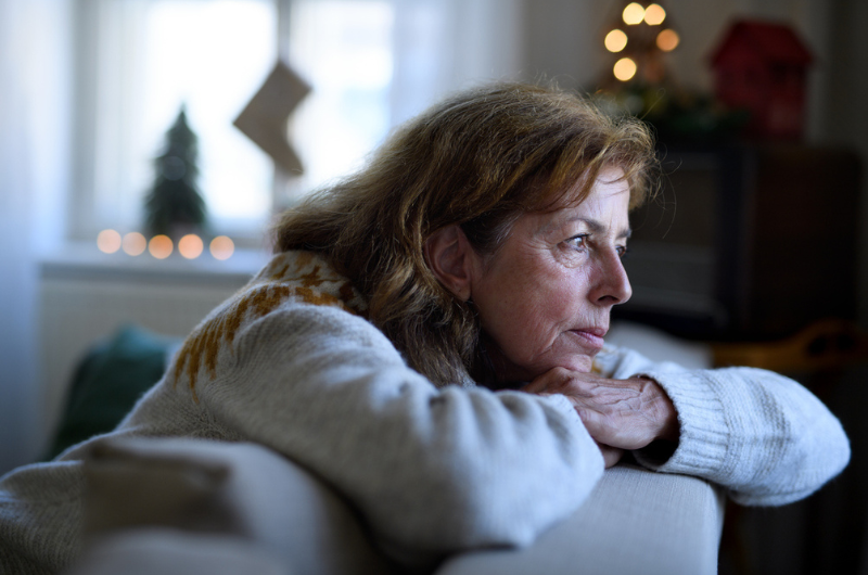 Portrait of lonely senior woman sitting on sofa indoors during the holidays.