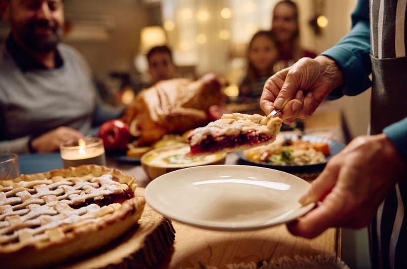 Close up image of a senior woman serving Thanksgiving pie to her family at dining table.