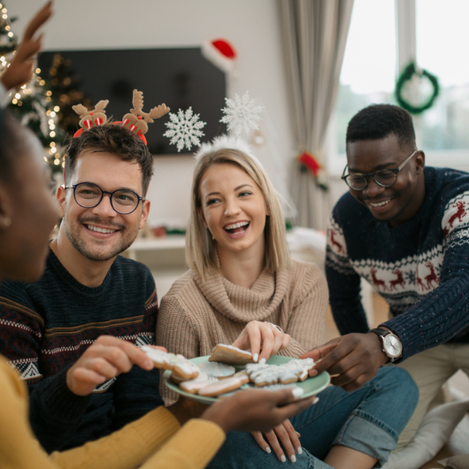 Diverse group of friends eating Christmas themed cookies and smiling.