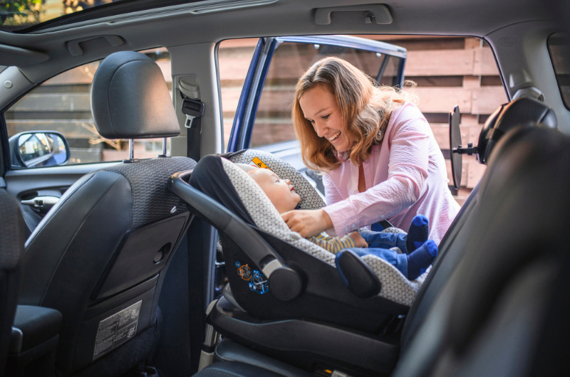 Mother putting her baby boy into a car safety seat.