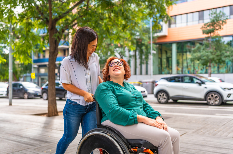 Woman with a disability talks with a friend while she is pushing her wheelchair along the city.