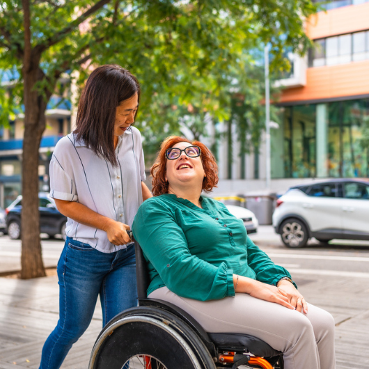 Woman with a disability talks with a friend while she is pushing her wheelchair along the city.