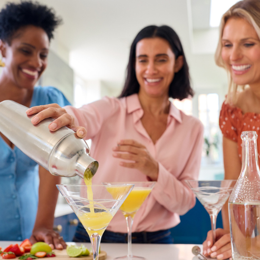 Three mature female friends are at home mixing mocktails together.