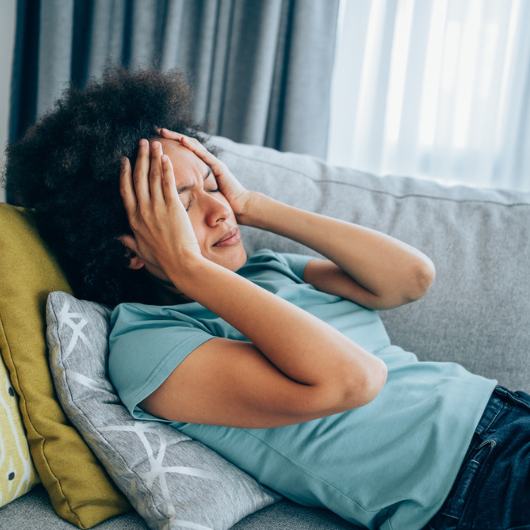 Young woman is lying on the couch and holding her head with hands.