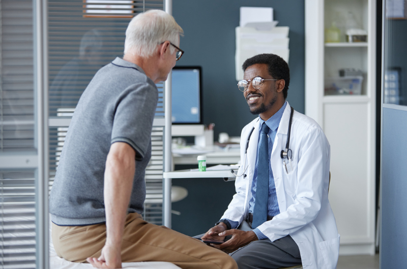 Friendly African American doctor wearing glasses and smiling while listening to senior patient.