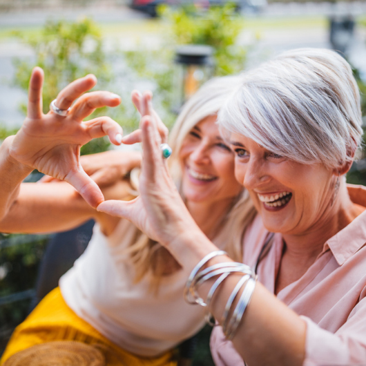Fashionable senior friends having fun at a restaurant and making a heart symbol with their hands.
