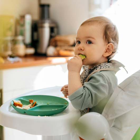 Cute blond baby girl eating a meal while sitting in a high chair.