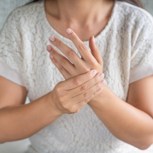 Close-up of a young woman sitting on sofa dealing with a numb hand.
