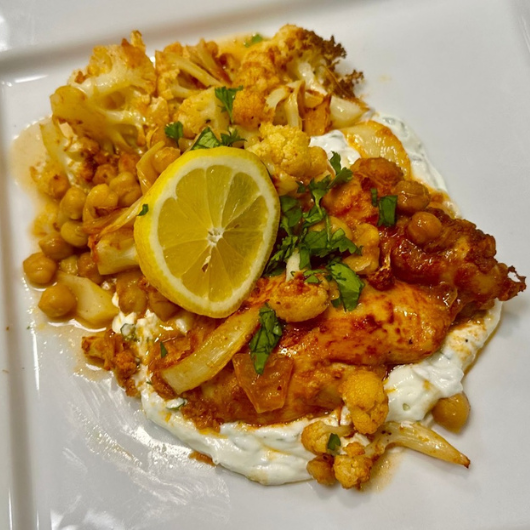 Top-down view of a dish featuring chicken thighs, cauliflower and flavorful herbs and spices.