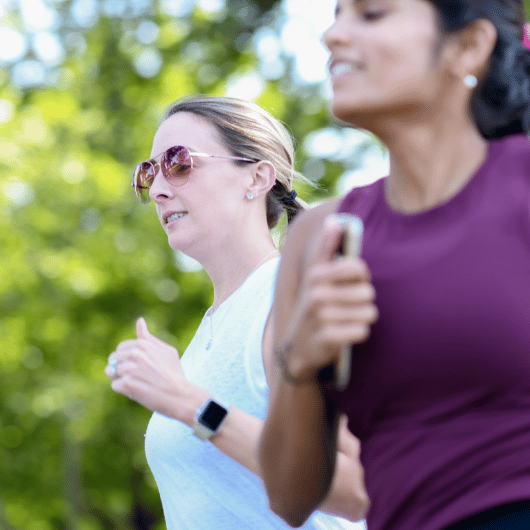 Two young women run outdoors side-by-side.