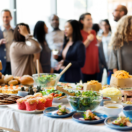 A buffet table full of food is shown with a small group of people in the background.