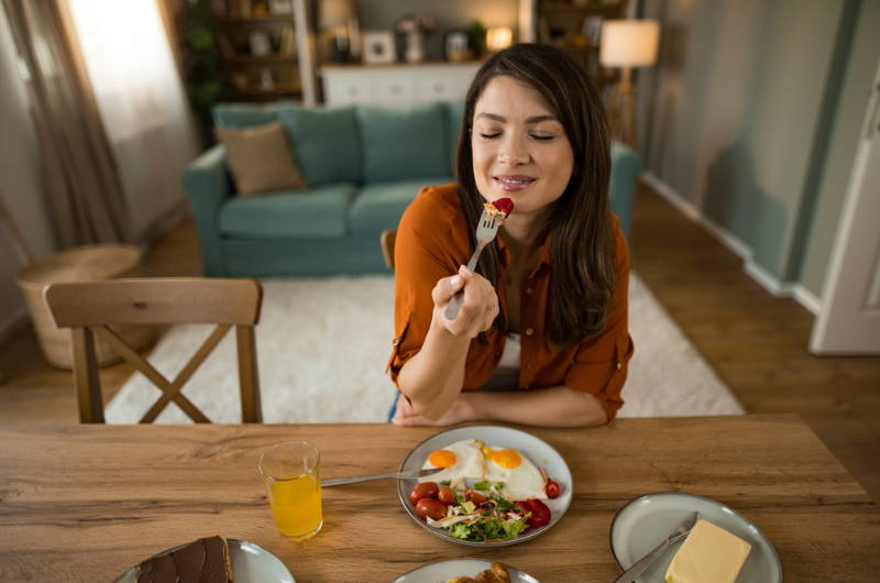  Happy woman eats breakfast at home and enjoys the taste.