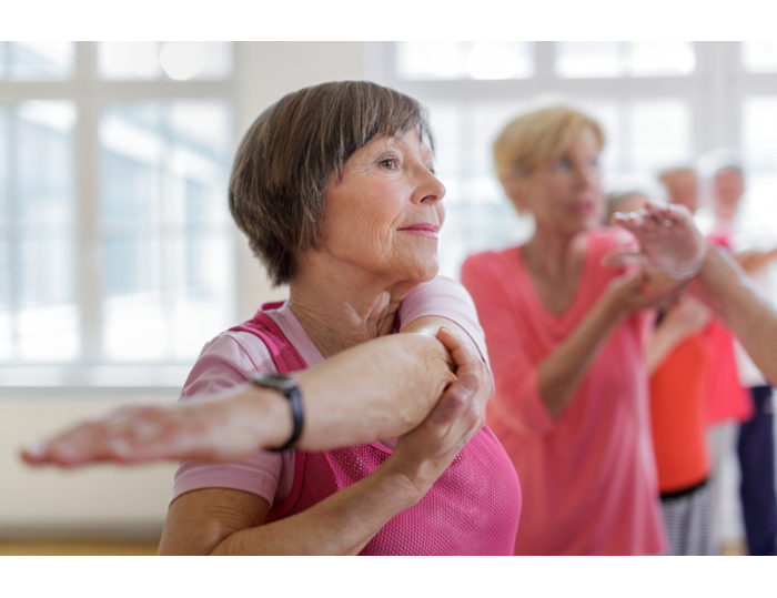 A senior woman stretches her arm in a group class.