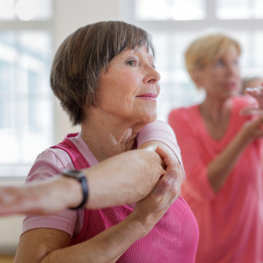 A senior woman stretches her arm in a group class.  