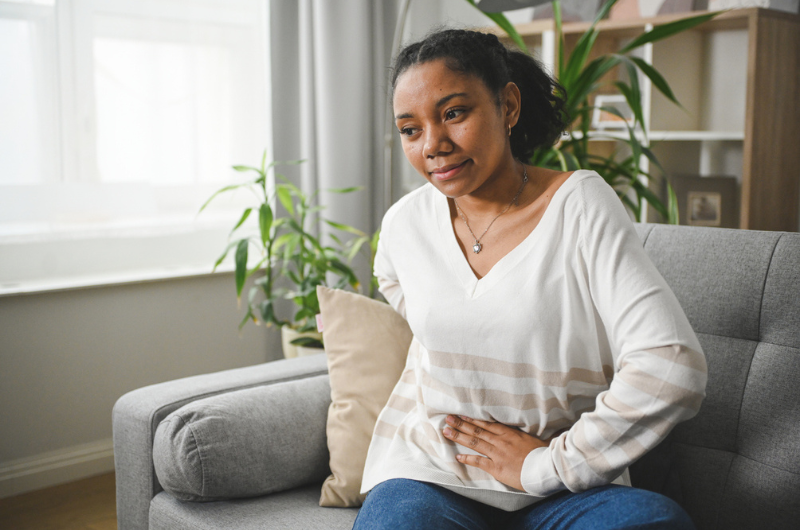  Young adult woman clutches her stomach.