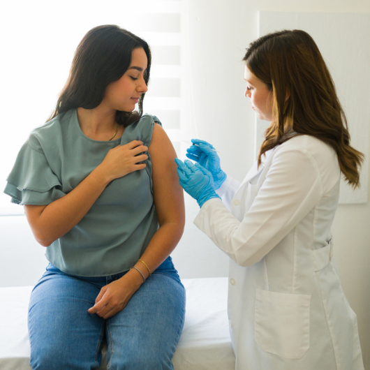 Doctor in gloves is administering allergy shots to a young woman in a medical office.