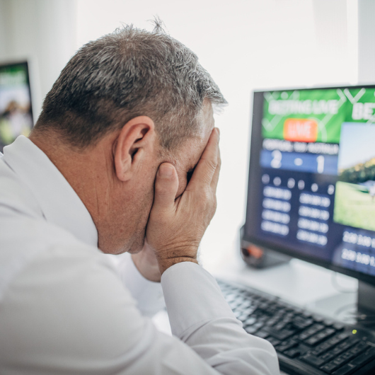 Older man with his face in his hands is doing sports betting using a computer.  