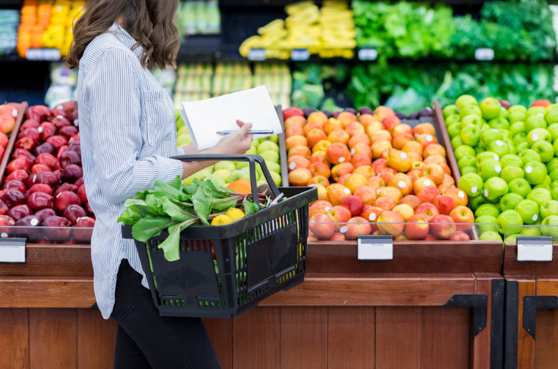 Young woman carries a shopping basket filled with fresh produce. 