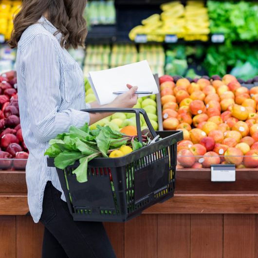 Young woman carries a shopping basket filled with fresh produce.