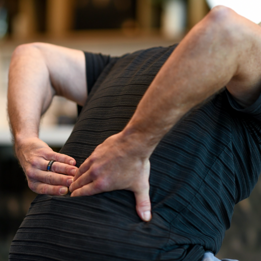 A middle-aged man leans forward and clutches his lower back.