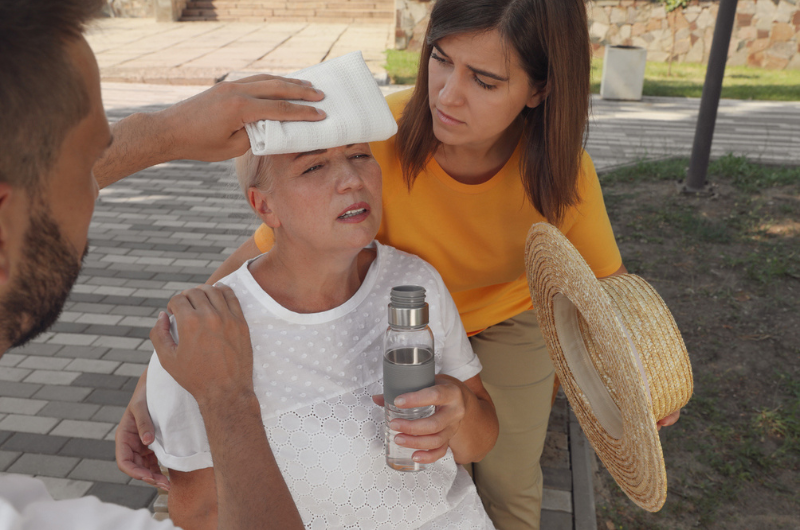 People helping mature woman on city street suffering from heat stroke.