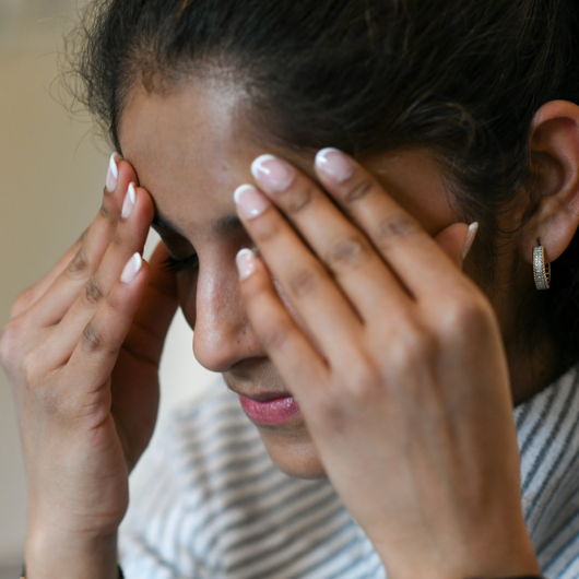 A young woman holds her hands to her head in pain.