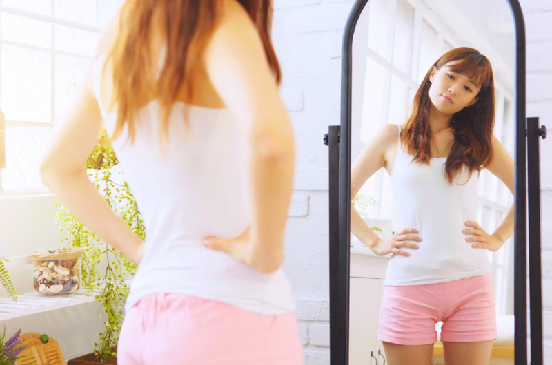 An Asian teen girl looks at herself in a full-length mirror.