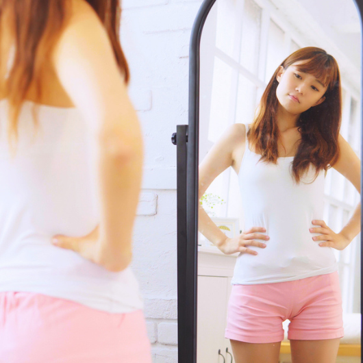 An Asian teen girl looks at herself in a full-length mirror.