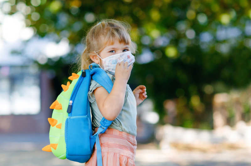 Toddler girl on her way to school while wearing a medical mask.