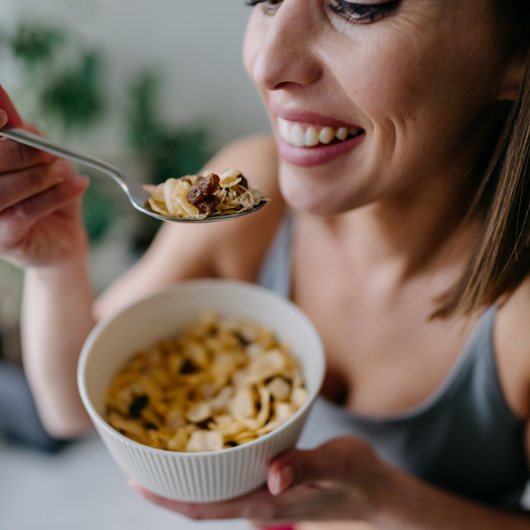Cheerful young woman in sportswear smiling while enjoying a bowl of cereals with raisins.